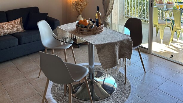 Een gezellige woonkamer met een bank, een bijzettafeltje met een fruitschaal, en een aan de muur bevestigde televisie.