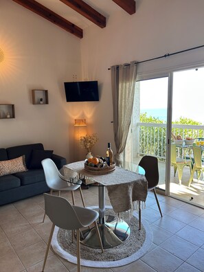 A cozy living room with a sofa, a coffee table with a fruit basket, and a TV mounted on the wall. - air-conditioned T1 apartment for 2 people, terrace with sea view, garden & parking (Monticello)