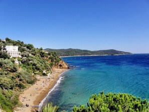 Eine Küstenansicht mit Strand, klarem blauen Meer und einer Hügelkuppe mit Gebäuden.
