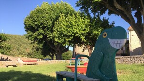 Un parque con una escultura verde de una figura similar a un dinosaurio, un banco rojo y un muro de piedra.