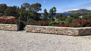 Eine Küstenlandschaft mit einer Steinmauer, Kiesgrund und Blick auf das Meer und ferne Hügel.