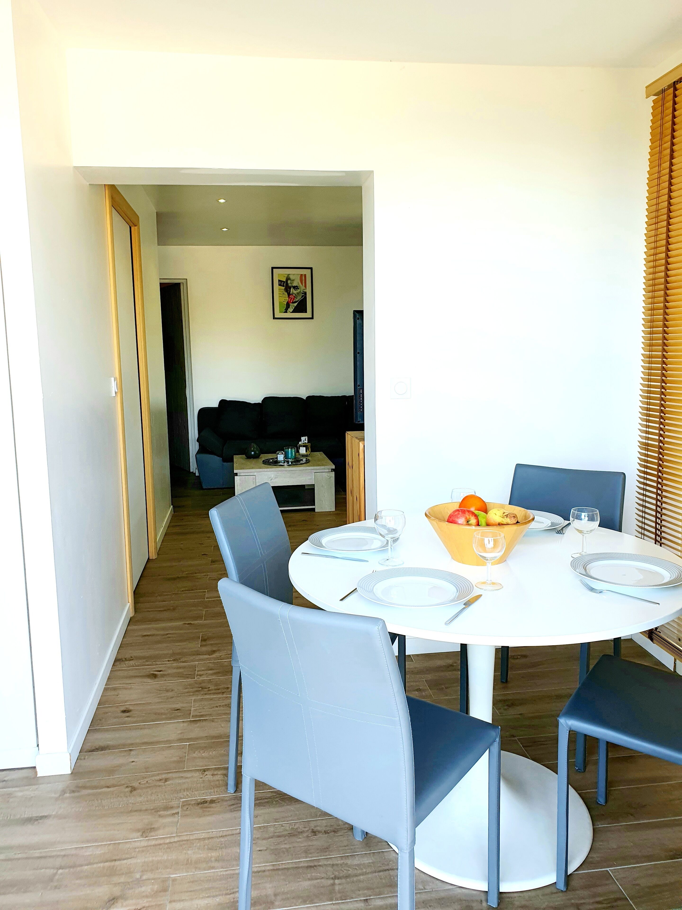 A dining area with a round table set for four, surrounded by chairs. A bowl of fruit and glasses are on the table.