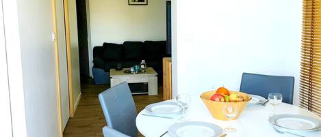 A dining area with a round table set for four, surrounded by chairs. A bowl of fruit and glasses are on the table.