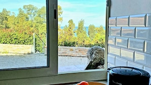 Eine Küche mit Blick auf einen Garten und eine Steinsäule, ein Kaffeeautomaten, eine Schüssel mit Obst und eine Tasse auf der Arbeitsfläche.