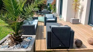 An outdoor patio with wicker furniture, a palm tree, and a building in the background.
