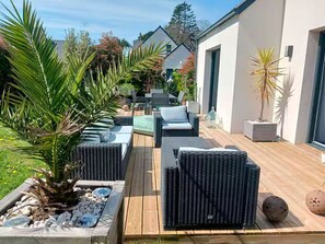 An outdoor patio with wicker furniture, a palm tree, and a building in the background.