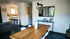 A modern dining area with a wooden table, white chairs, and a kitchen in the background.
