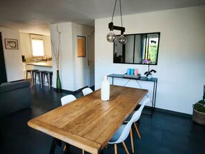 Zona pranzo moderna con tavolo in legno, sedie bianche e cucina sullo sfondo.