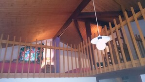 Een houten balkon met een leuning, een hanglamp en een raam met bloemen gordijnen.