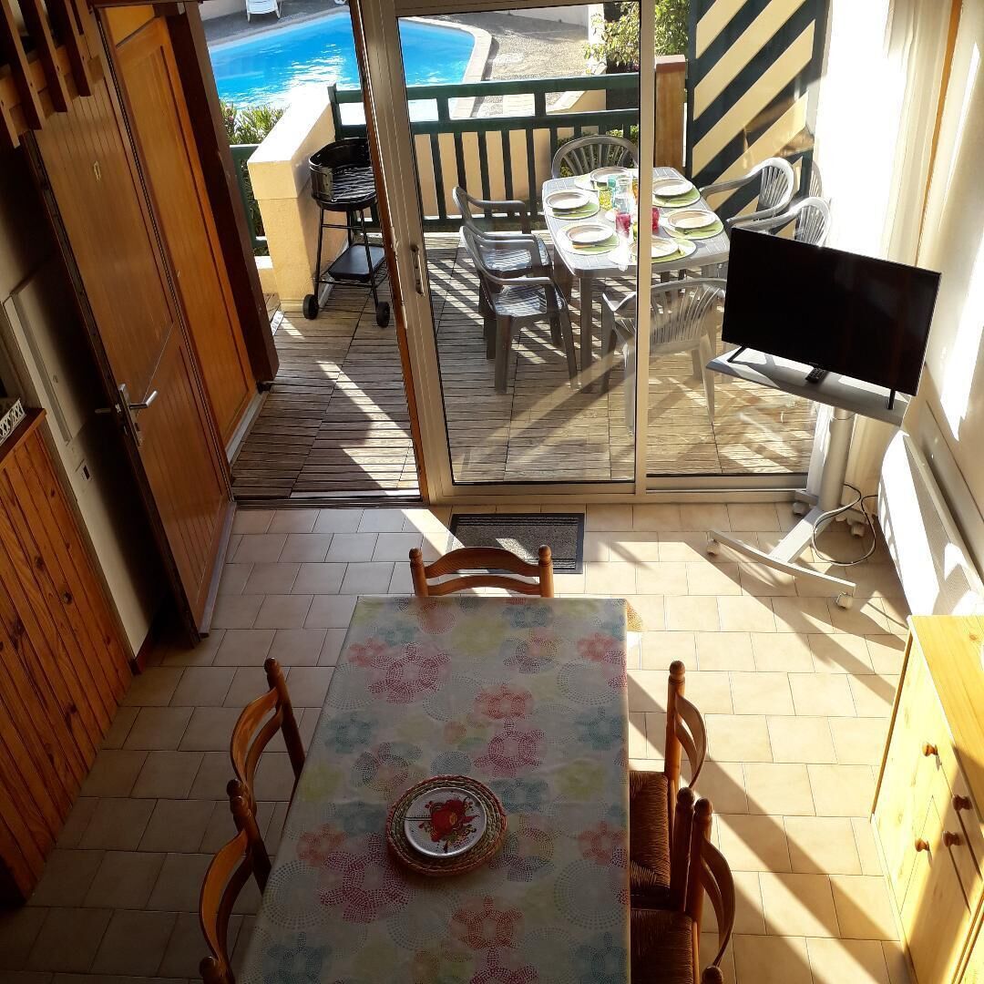 Un espace extérieur aménagé avec une table, des chaises, un téléviseur et une vue sur une piscine.