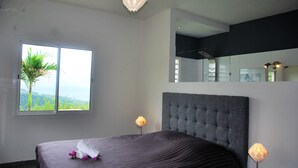 Une chambre à coucher moderne avec un grand lit, une fenêtre donnant sur un paysage verdoyant et un miroir au mur.