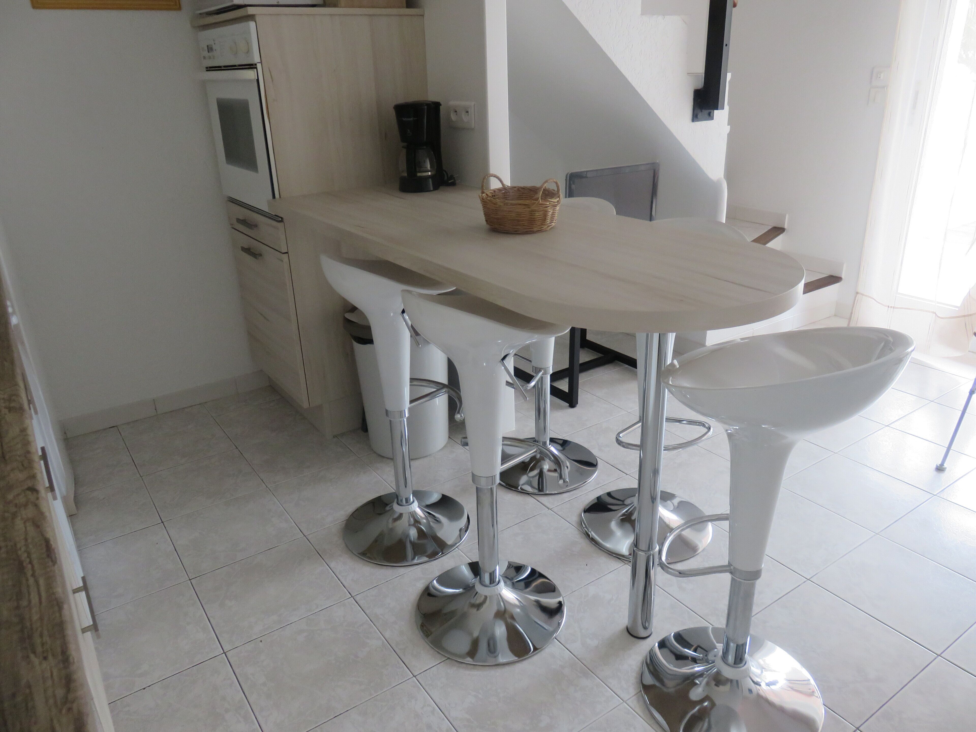 A modern kitchen with white cabinets, a coffee maker, and a dining area with bar stools.