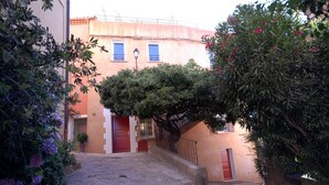 A narrow stone-paved alleyway with a building featuring a red door and a small window.
