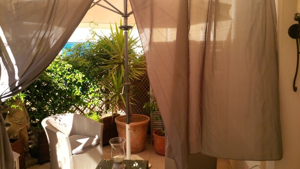 Eine Terrassenfläche mit einem weißen Stuhl, einem kleinen Tisch mit einem Glas und Topfpflanzen.