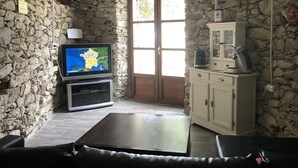 A stone-walled room with a television, a cabinet, and a door. - Authentic village house: charm, tranquility, and nature, just 15 minutes from Saint-Florent (Saint-Florent)