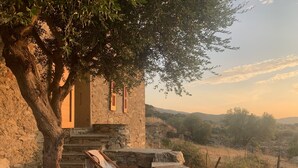 A stone building with a wooden chair and a table, a potted plant, and a view of the countryside. - Authentic village house: charm, tranquility, and nature, just 15 minutes from Saint-Florent (Saint-Florent)