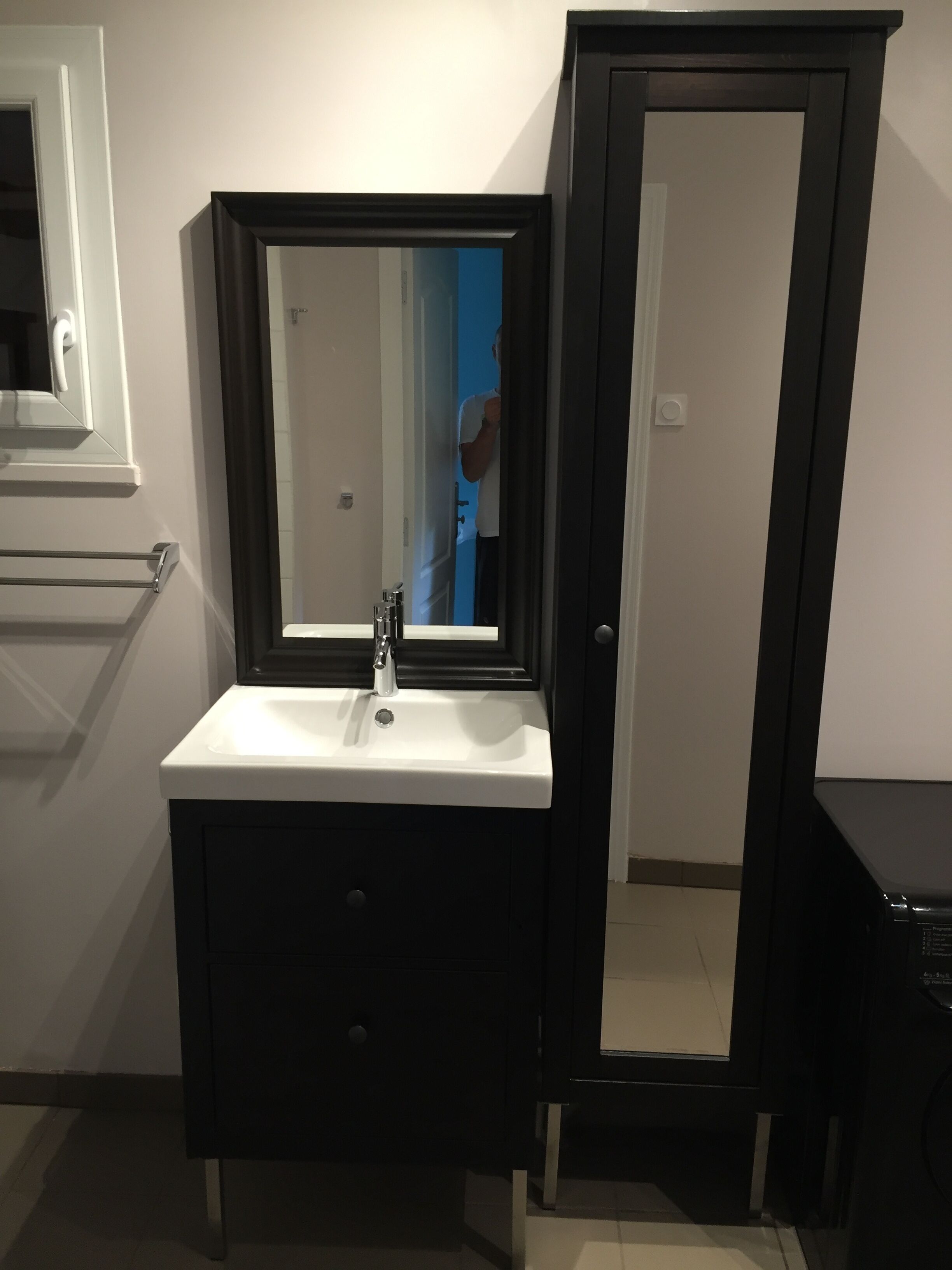 A bathroom with a white sink, a dark vanity, a large mirror, and a door.