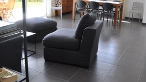 Una sala de estar moderna con un sofá gris, una mesa de comedor con sillas y vistas al exterior.