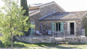 A stone house with a balcony, a tree in the foreground, and a clear sky.