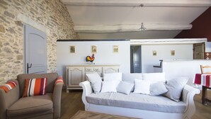 A cozy living room with a stone wall, a white sofa, a beige armchair, and a wooden coffee table.