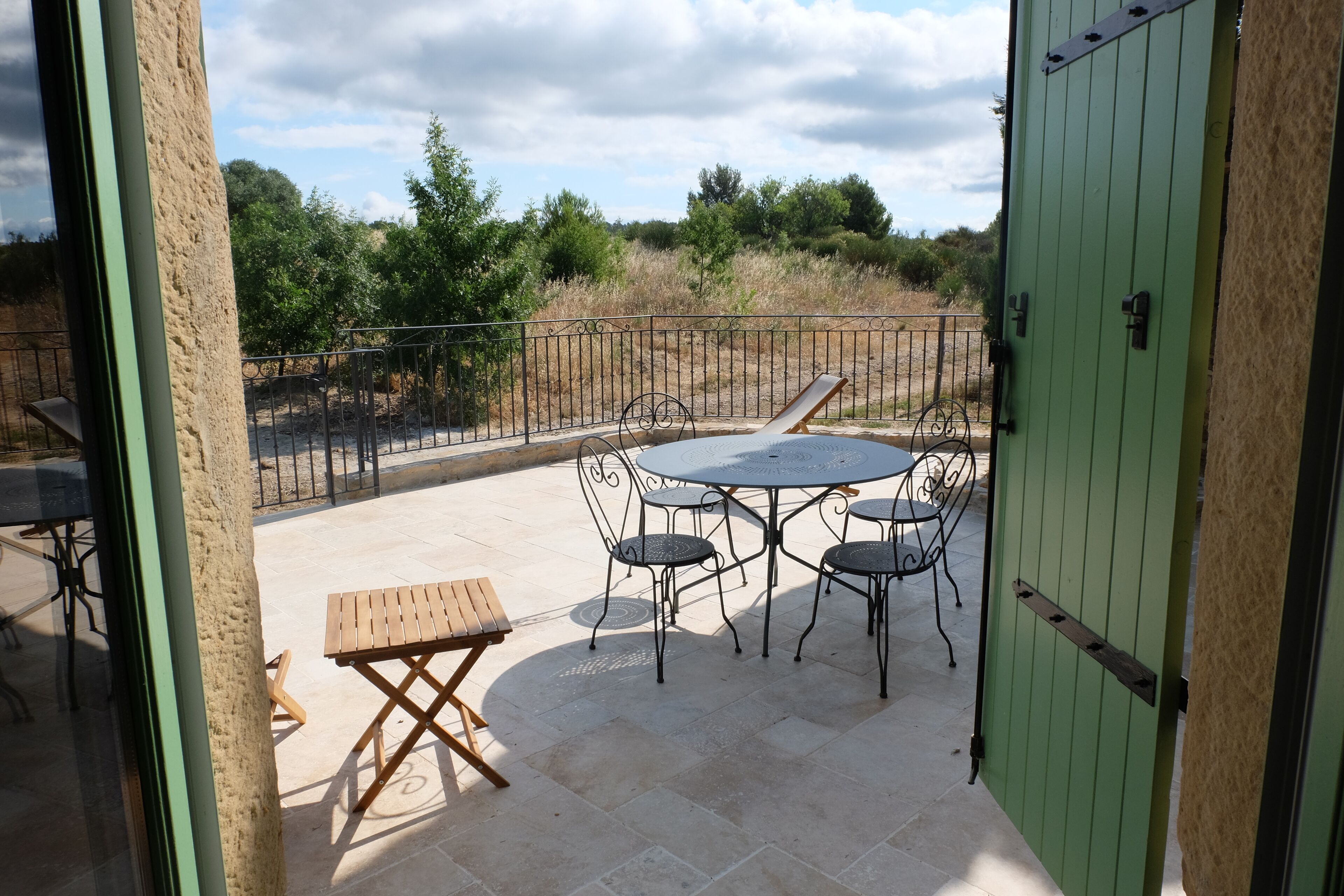 An outdoor patio with a round table and chairs, a wooden bench, and a green door.