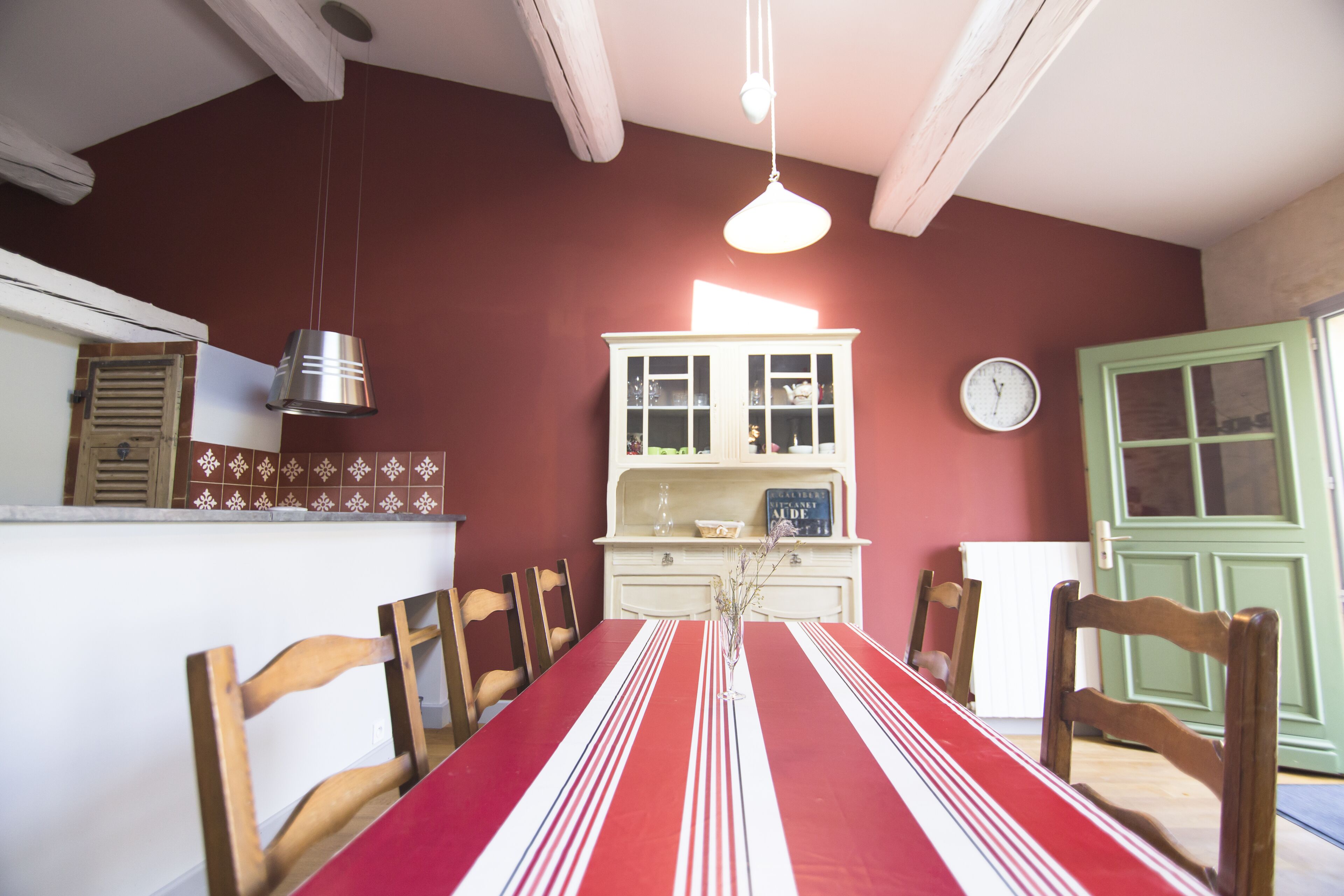 A dining area with a red-striped table, wooden chairs, a white cabinet with glass doors, and a green door.