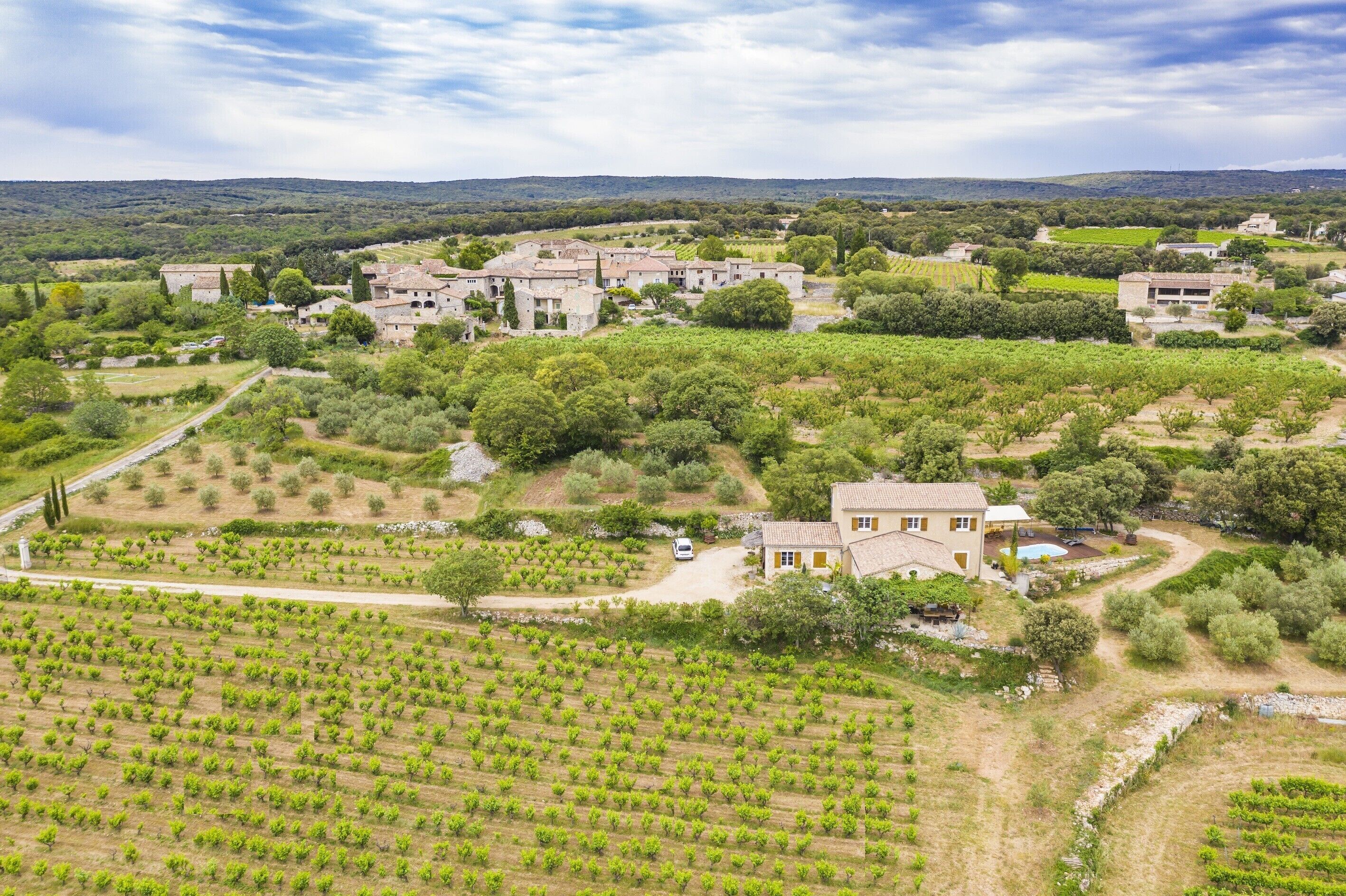 Un vignoble avec des rangées de vignes, un bâtiment en pierre avec un toit de tuiles et un bâtiment plus petit avec une façade jaune.