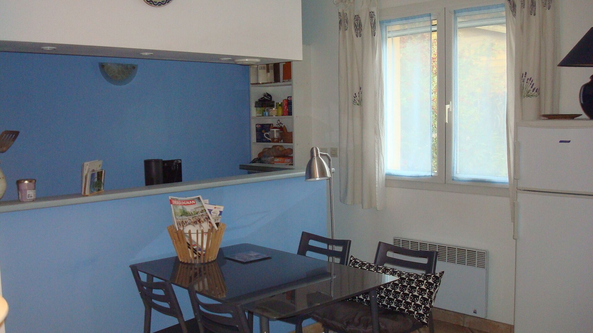 Une cuisine de taille réduite avec un mur bleu, une table à manger avec des chaises et une fenêtre avec des rideaux.