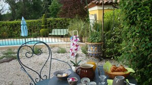 A round metal table with a breakfast setup including croissants, a jug of orange juice, and jars of jam. - Country cottage fully furnished, in private property, quiet. (Draguignan)