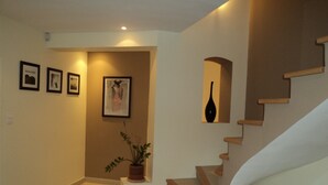 Una escalera con escalones de madera y una pared blanca. Hay cuadros enmarcados en la pared y una planta en maceta cerca de la base de la escalera.