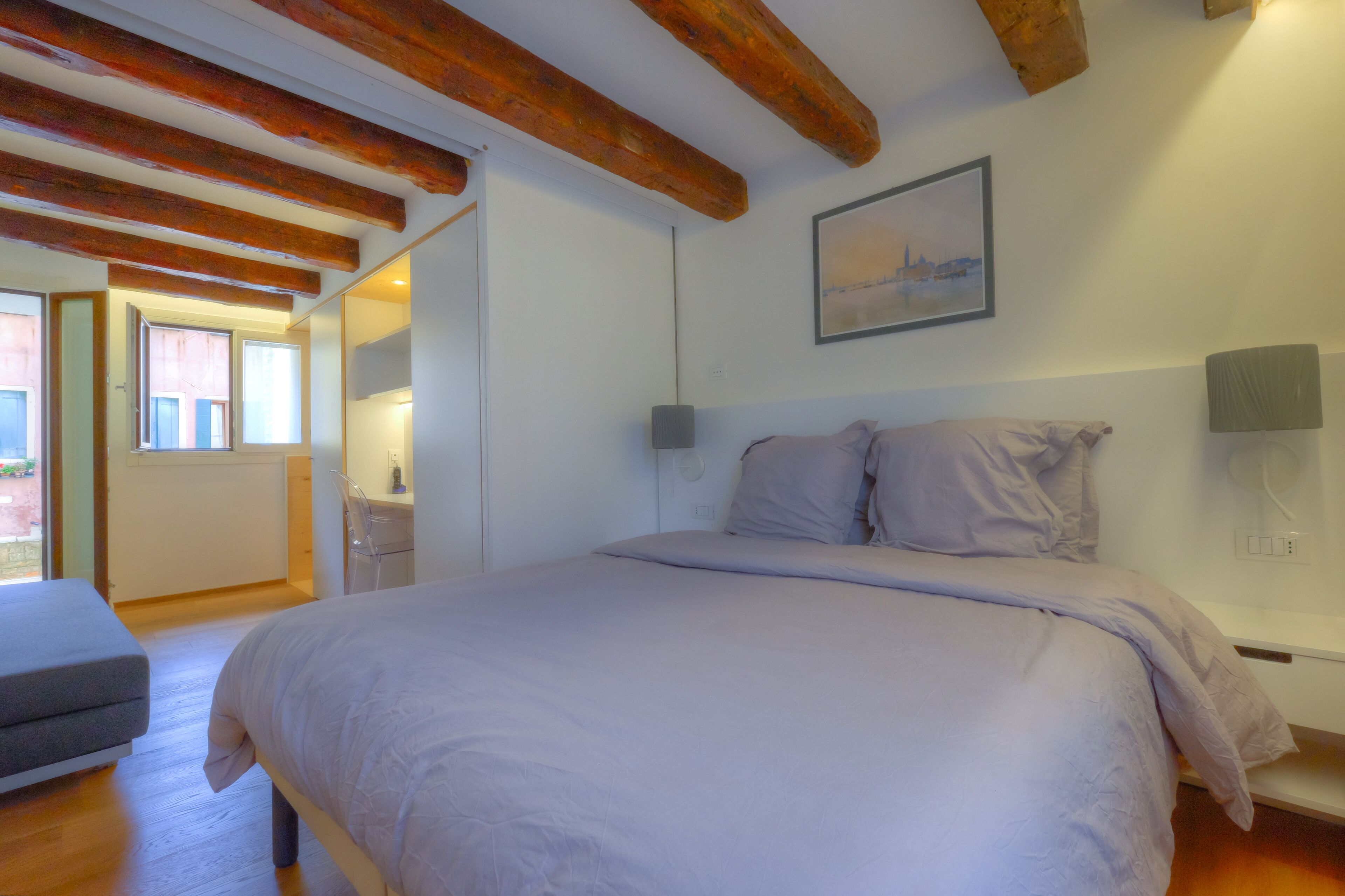 Quarto com cama grande, vigas de madeira, escrivaninha e janela.