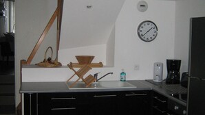 Une petite cuisine équipée d’un évier, d’une horloge et d’une machine à café.
