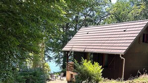 Une cabane rustique en bois, surmontée d’un toit en métal, entourée d’une végétation luxuriante et accessible par un sentier de terre.