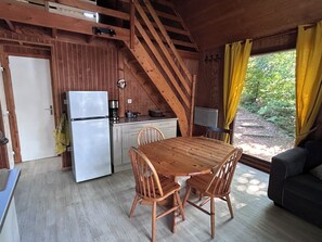L’intérieur d’un chalet en bois comprend une cuisine, une table à manger et des chaises, un escalier et une vue sur la forêt.