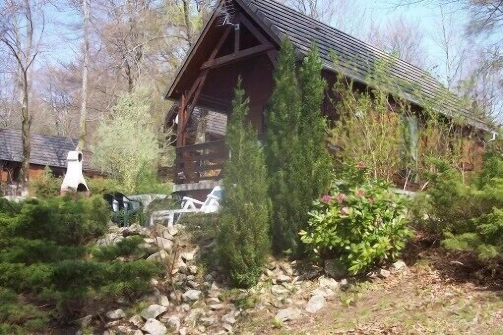 Eine rustikale Blockhütte mit steilem Dach, umgeben von dichten Nadelbäumen und einem Steinweg, der zum Eingang führt.