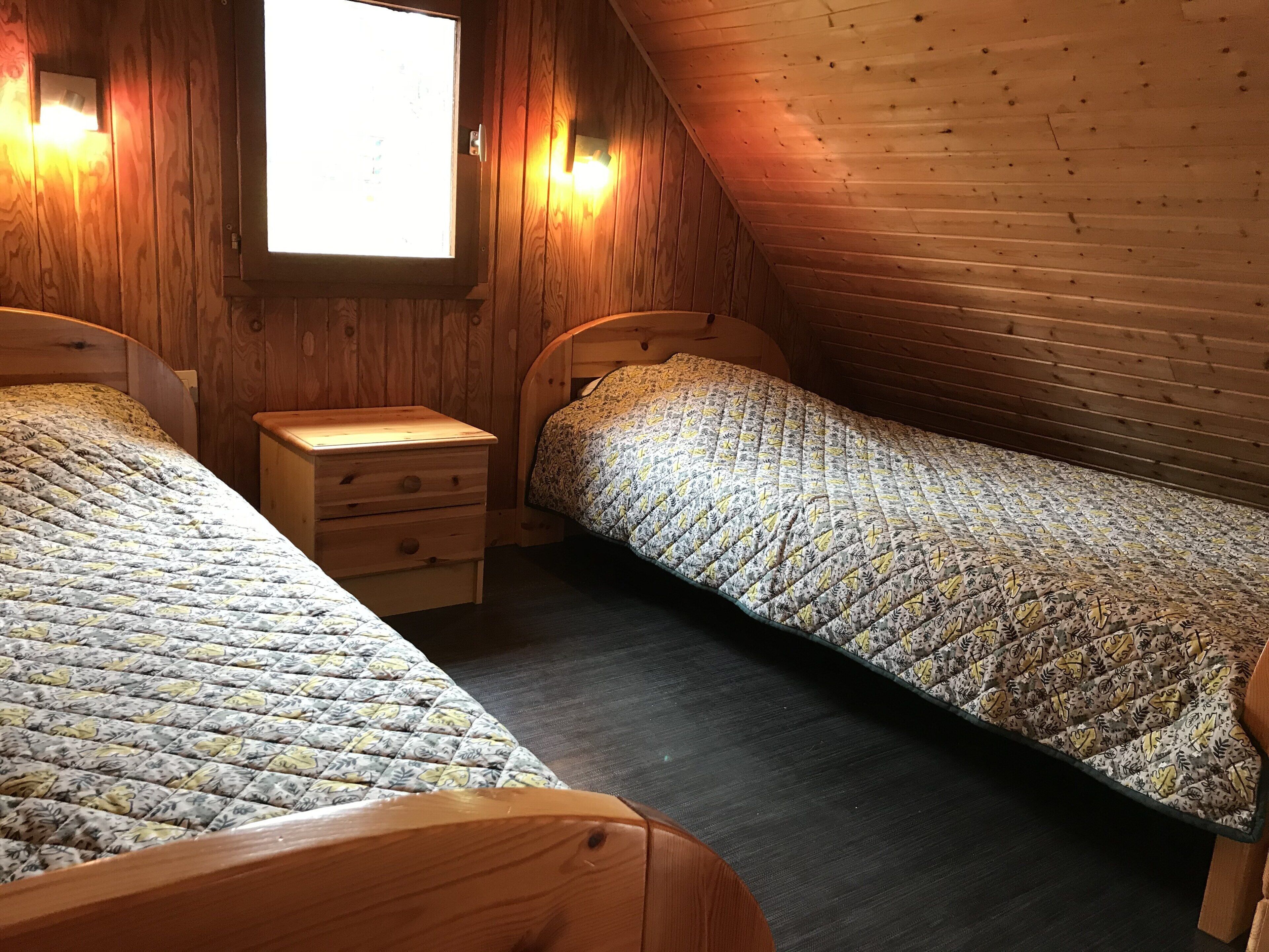 Ein kleines, gemütliches Zimmer mit zwei hölzernen Betten, einem Nachttisch und einem Fenster.