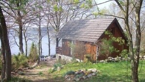 Un chalet rustique avec un toit en pente, entouré d’arbres et accessible par un chemin de gravier.