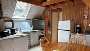 Une cuisine compacte avec une table et des chaises en bois, un four encastré, un lave-vaisselle et un réfrigérateur.