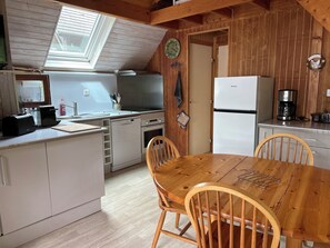 Una cocina compacta con una mesa y sillas de madera, horno empotrado, lavavajillas y refrigerador.