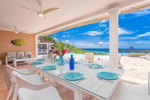 A dining area with a table set for six, overlooking a pool and ocean view.