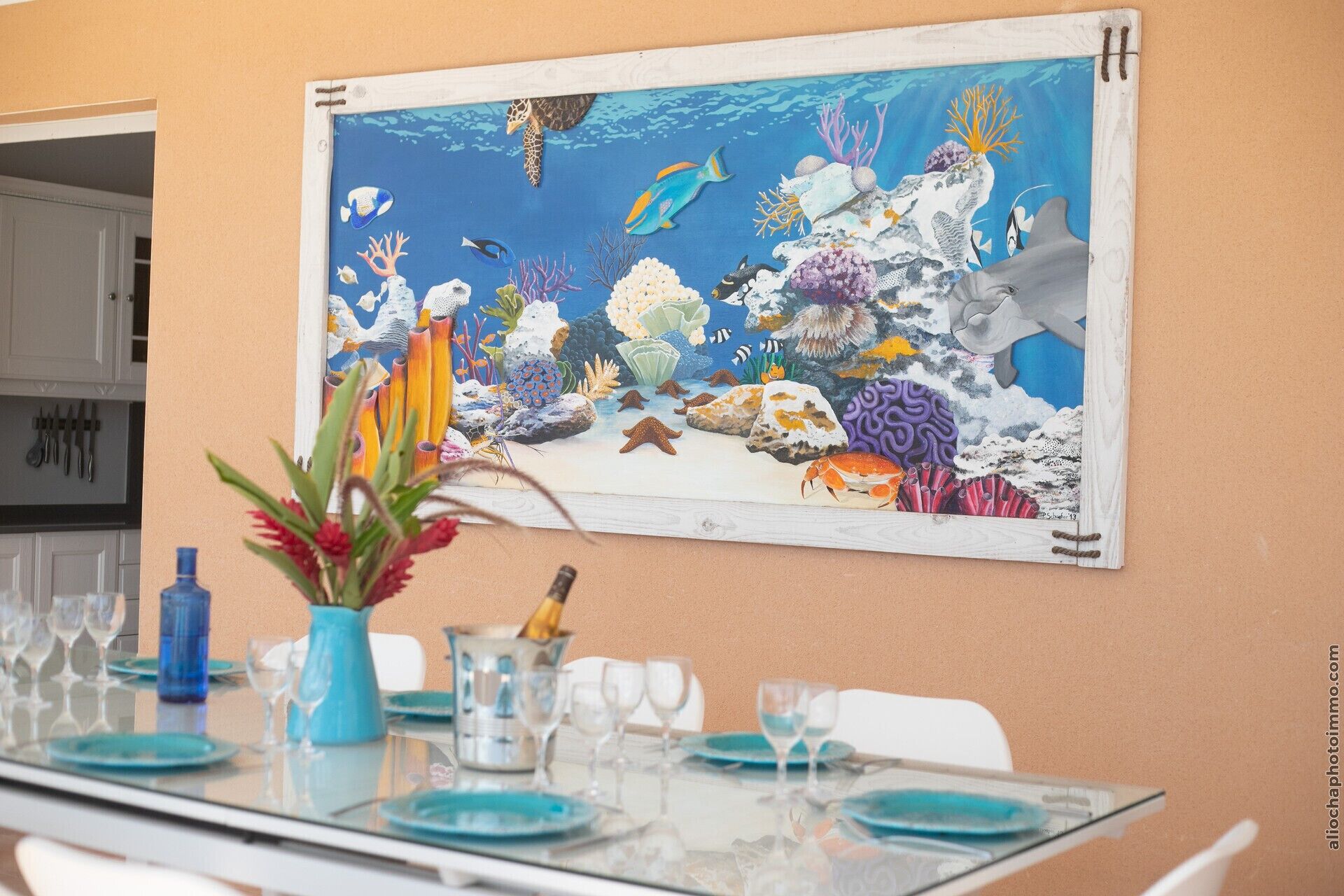 Un comedor con una mesa preparada para cuatro personas, que presenta un cuadro grande con motivos marinos en la pared.