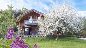 Une cabane en bois dotée d’un balcon, entourée d’une végétation luxuriante et d’arbres en fleurs.