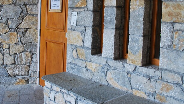 Un edificio de piedra con puerta de madera y tres ventanas.