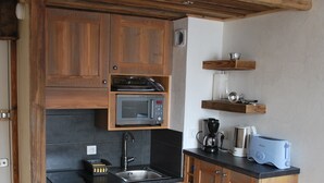 Una cocina compacta con armarios de madera, microondas integrado, un lavabo, cafetera y tostadora.