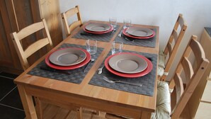 Una mesa de comedor de madera dispuesta con cuatro platos, cubiertos y vasos, rodeada de sillas de madera.