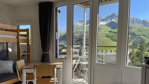 A room with a bunk bed, a wooden table, a chair, and a view of mountains through large windows. - Charming Studio 4 pers with south balcony and mountain view (Morzine)