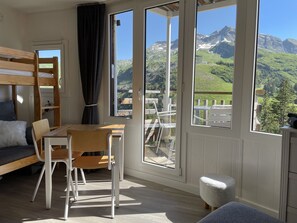 Une chambre avec un lit superposé, une table en bois, une chaise et une vue sur les montagnes par de grandes fenêtres.