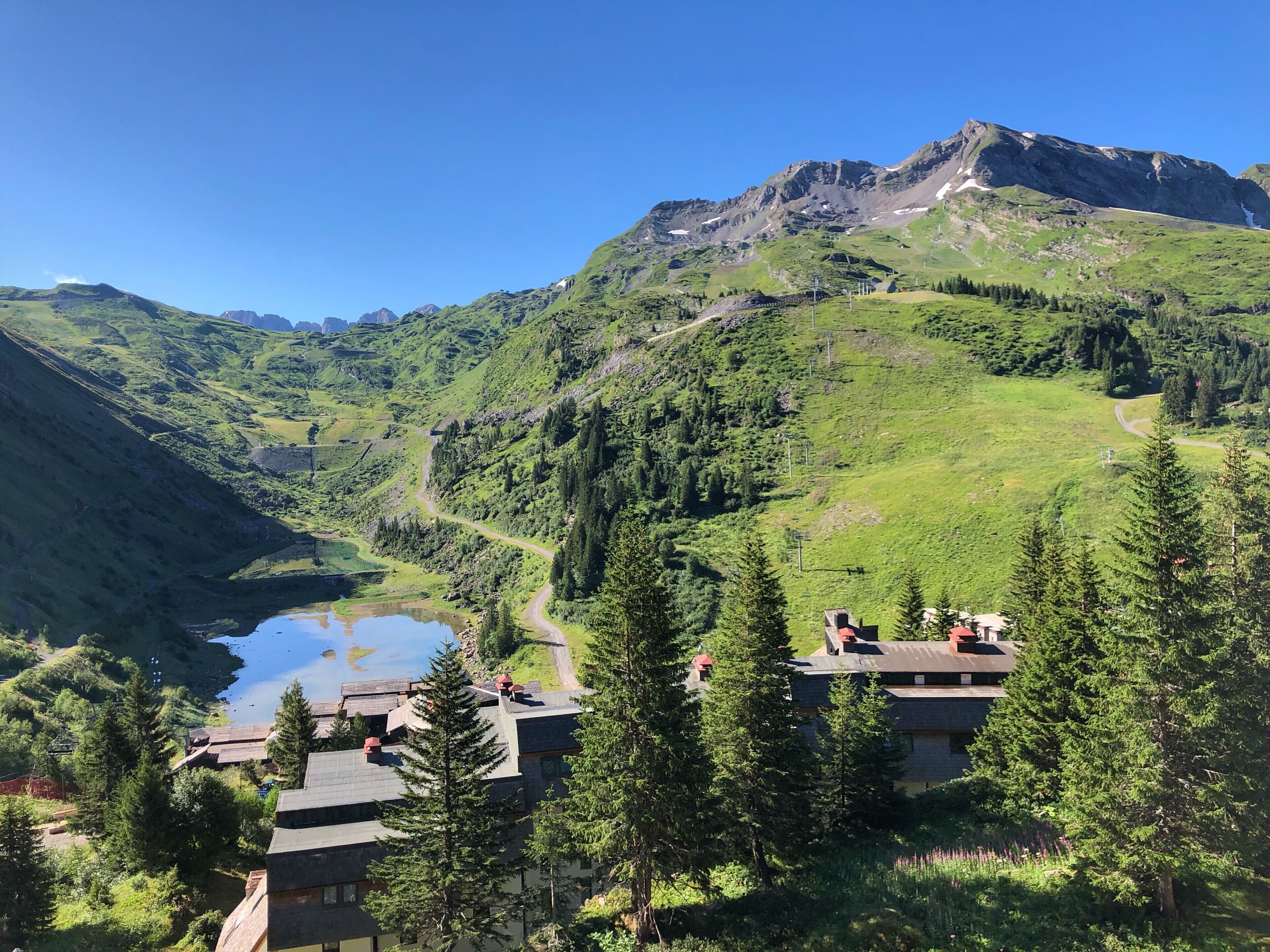Un refugio de montaña con varias construcciones, un lago y un camino sinuoso.