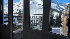 A room with a view of snow-covered mountains and a wooden deck outside. - Charming Studio 4 pers with south balcony and mountain view (Morzine)