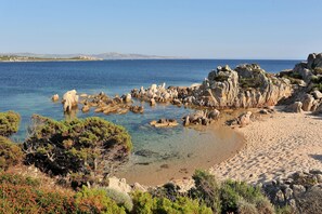 A coastal landscape with clear water, rocky formations, and sparse vegetation.
